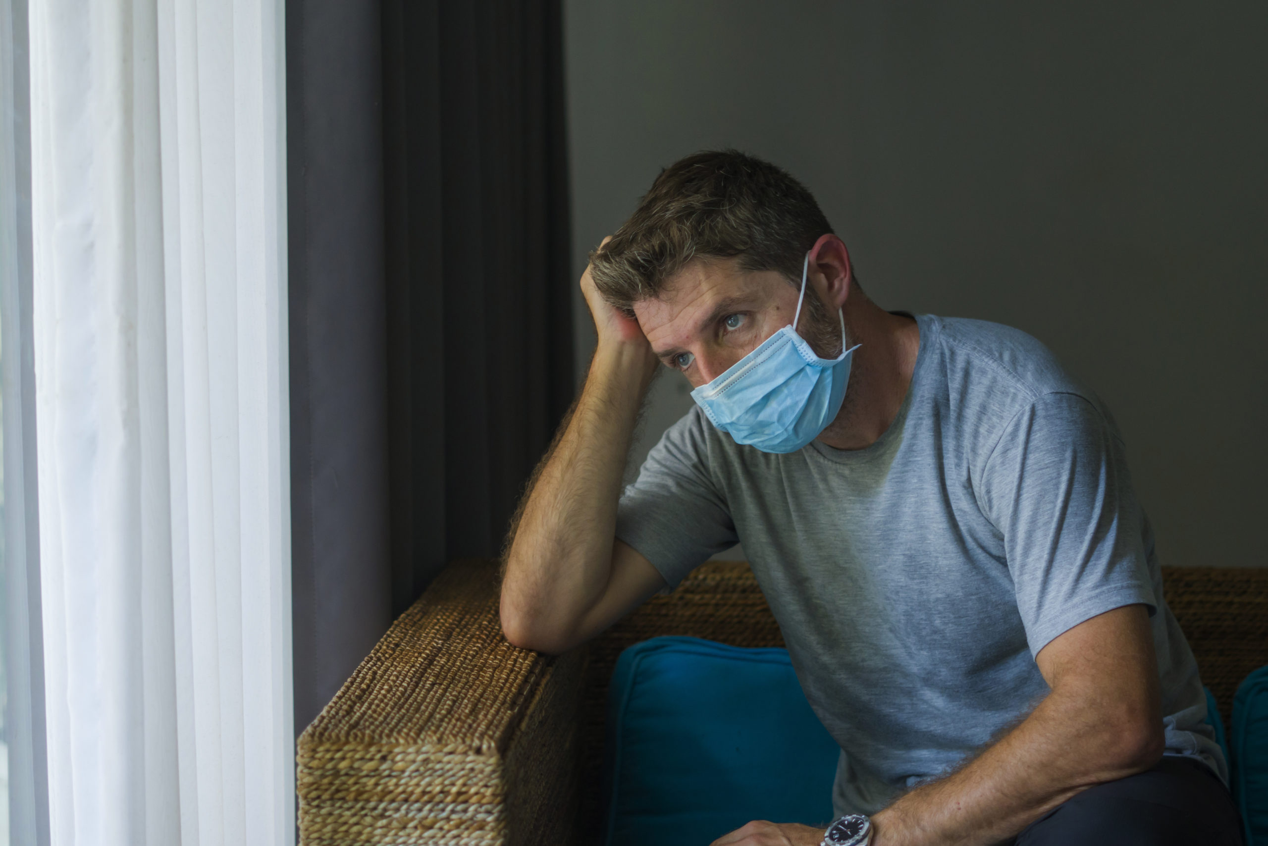 covid-19 virus lockdown - sad and worried man in medical mask thinking and feeling scared in quarantine following stay at home instructions to contain virus pandemic